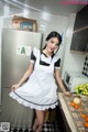 A woman in a maid outfit standing in a kitchen.