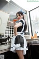 A woman in a maid outfit holding a carrot in a kitchen.