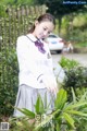 A woman in a school uniform standing next to a plant.