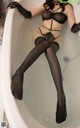 A woman sitting in a bathtub wearing black stockings and gloves.