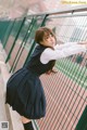 A woman in a school uniform leaning against a fence.