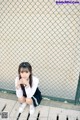 A young woman sitting on the ground in front of a fence.