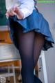 A woman in a blue skirt and black tights is standing in a classroom.