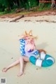 A woman in a bikini and hat sitting on a beach.