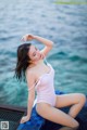 A woman in a white bathing suit sitting on a dock by the water.