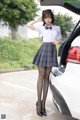 A woman in a school uniform standing next to a car.