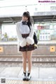 A woman in a school uniform standing on a train platform.