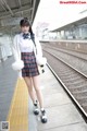 A woman in a school uniform standing on a train platform.