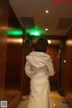 A woman in a white dress standing in an elevator.