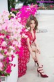 A woman in a red dress sitting on a wall with pink flowers.