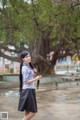 A woman with long black hair standing in front of a tree.